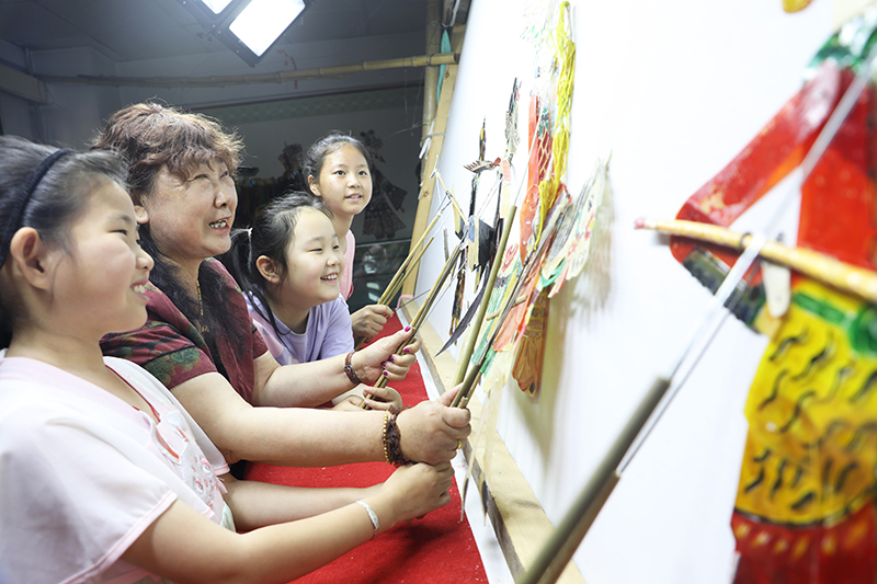 皮影藝人指導(dǎo)小朋友表演皮影戲。